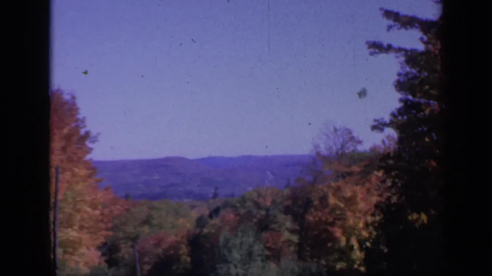 1959 Colorado landscape frame with soft-focus autumn woods, far hills, and dark window-like borders on 8mm film.