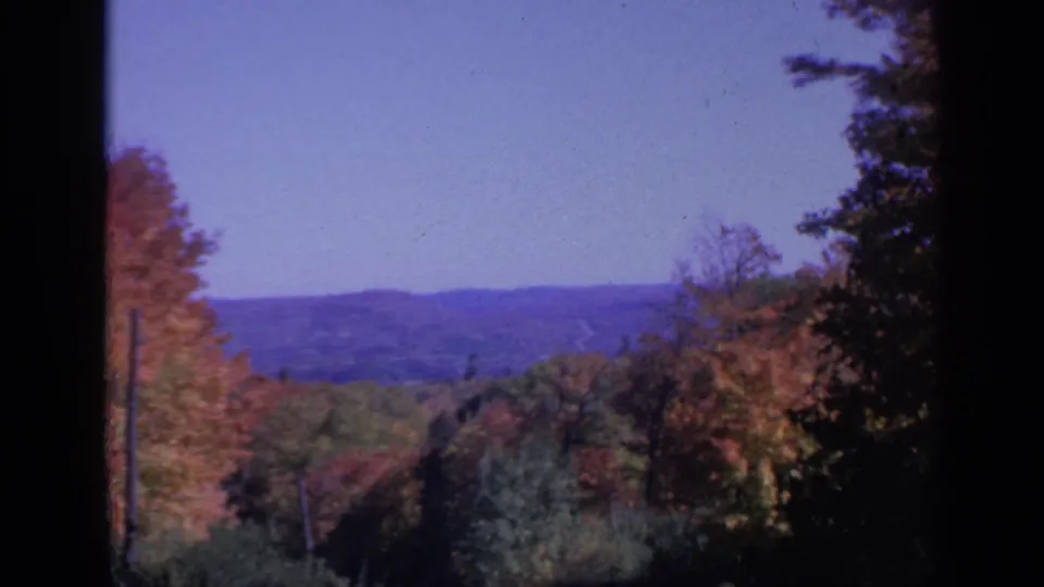 Colorado autumn landscape from 1959 with distant hills, rosy and gold foliage, dark framing edges, and visible 8mm film texture.