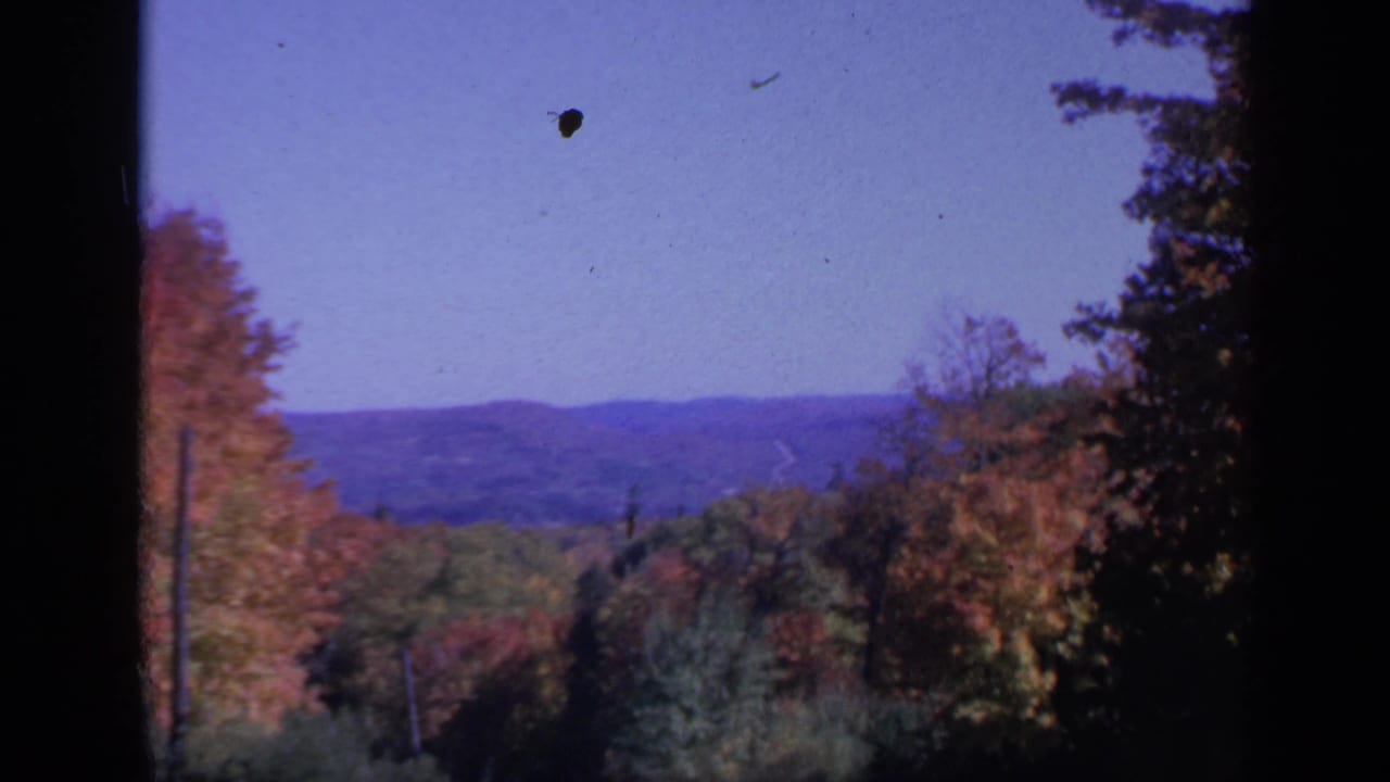 Autumn trees and distant hills under a blue sky, framed by dark film edges.
