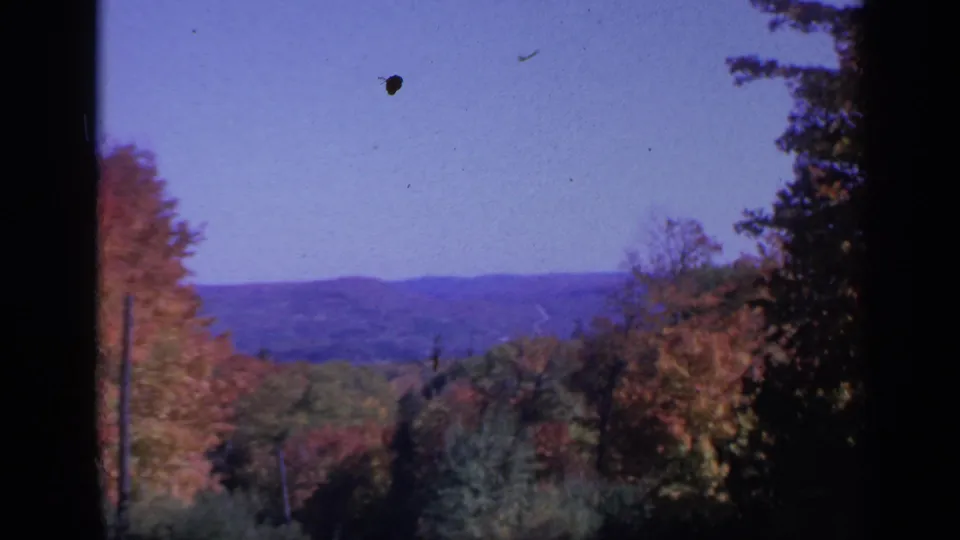 1959 Colorado home-movie frame showing fall foliage in a valley with rolling hills beyond and dark gate-edge framing.