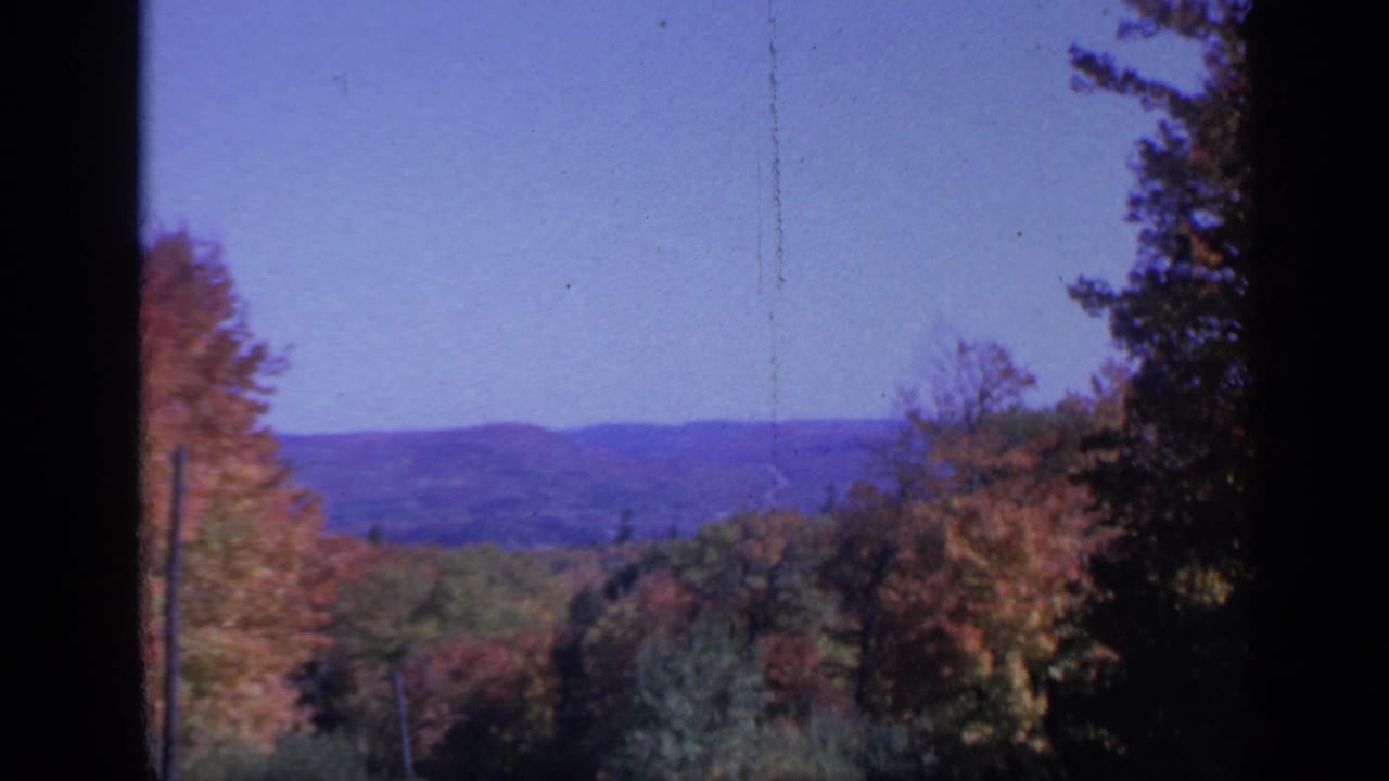 Colorado autumn landscape from 1959 with layered trees, distant low hills, and visible 8mm film grain and scratches.