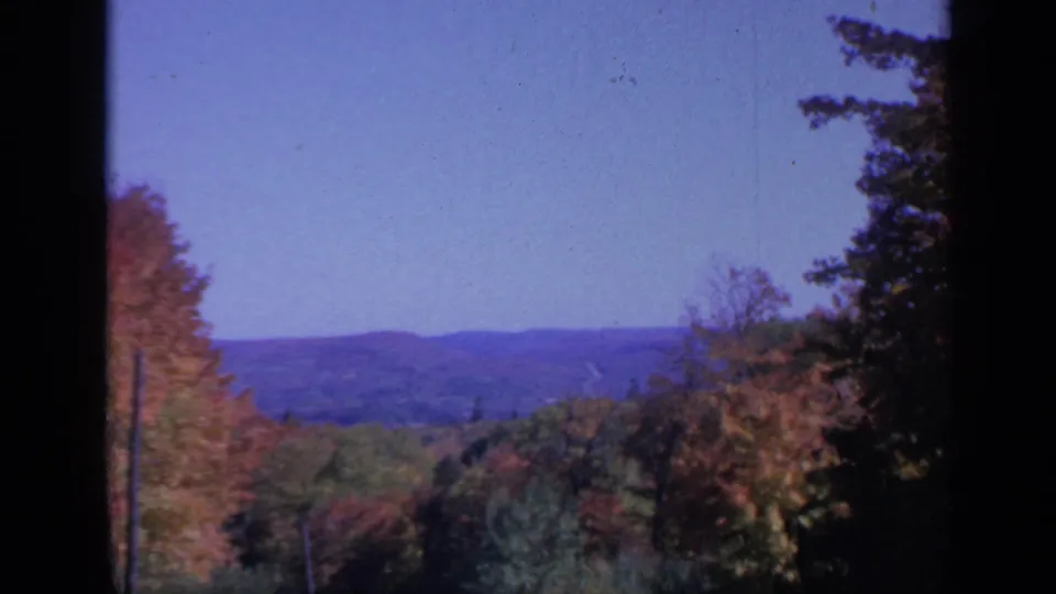 Vintage Colorado fall landscape frame with colorful treetops, hazy hills, blue sky, and pronounced film edge darkness.