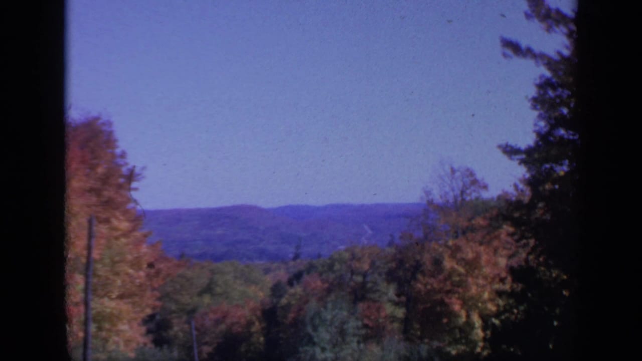 Autumn trees and distant blue ridges seen through dark window-like edges.