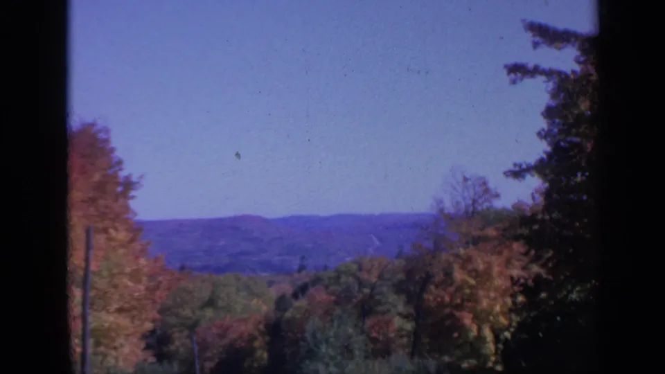 Vintage Colorado 8mm frame showing fall foliage, wooded hills, and a hazy distant ridge under open sky.