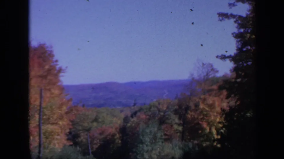 1959 Colorado home-movie frame of autumn woodland, distant hills, and dark edge framing from a traveler viewpoint.