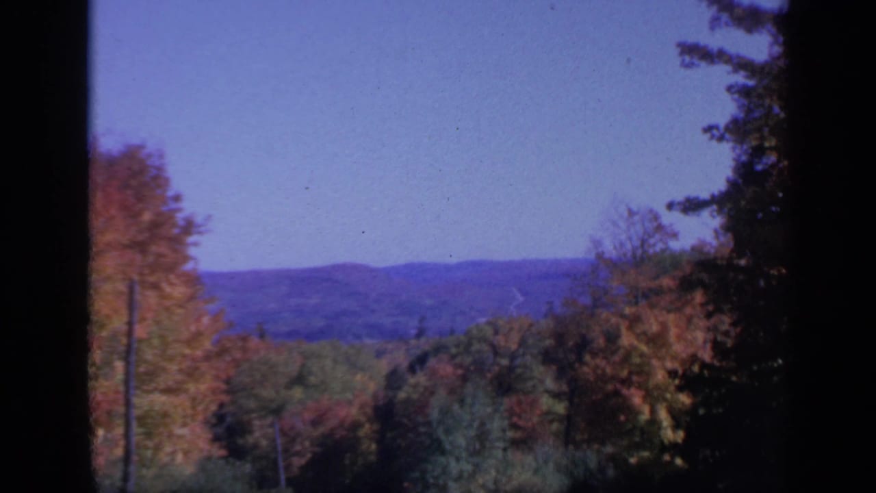 Autumn treetops and distant mountain ridges under a blue sky, framed by dark film edges.