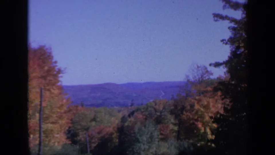 1959 Colorado 8mm frame showing fall-colored treetops, distant mountain terrain, blue sky, and dark edge vignetting.