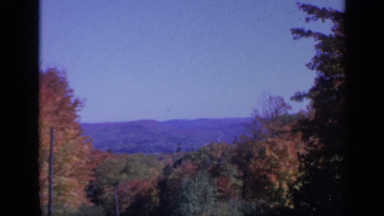 1959 Colorado home-movie frame with fall foliage in the foreground and a hazy mountain ridge across the horizon.
