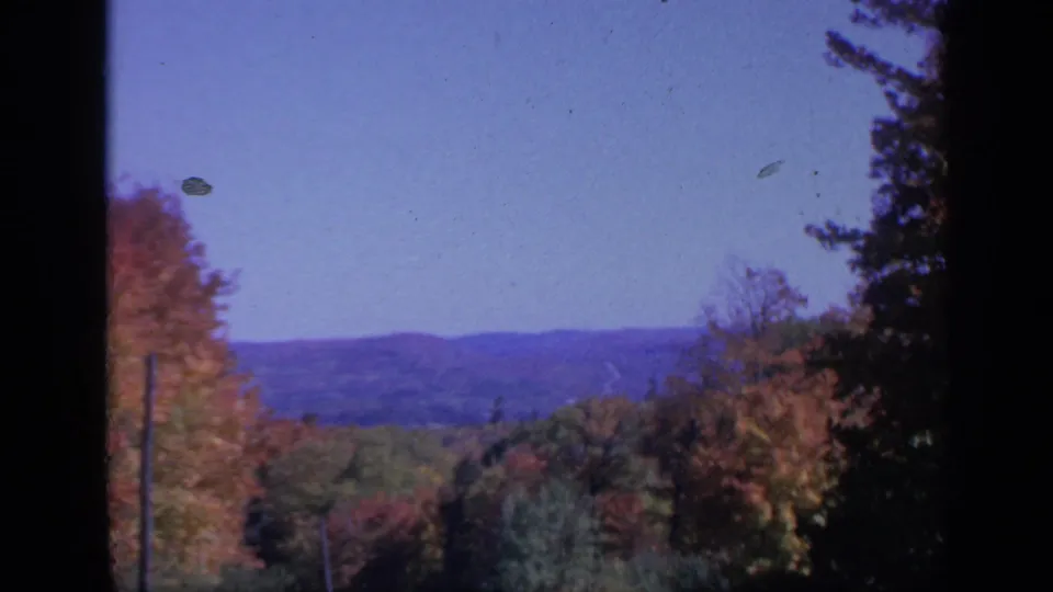 1959 Colorado 8mm still showing a wooded autumn valley, distant terrain, blue sky, and visible film dust.