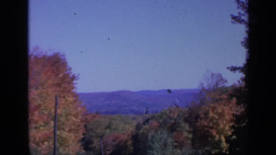 1959 Colorado frame with colorful treetops, a distant mountain horizon, soft focus, and dark 8mm frame edges.