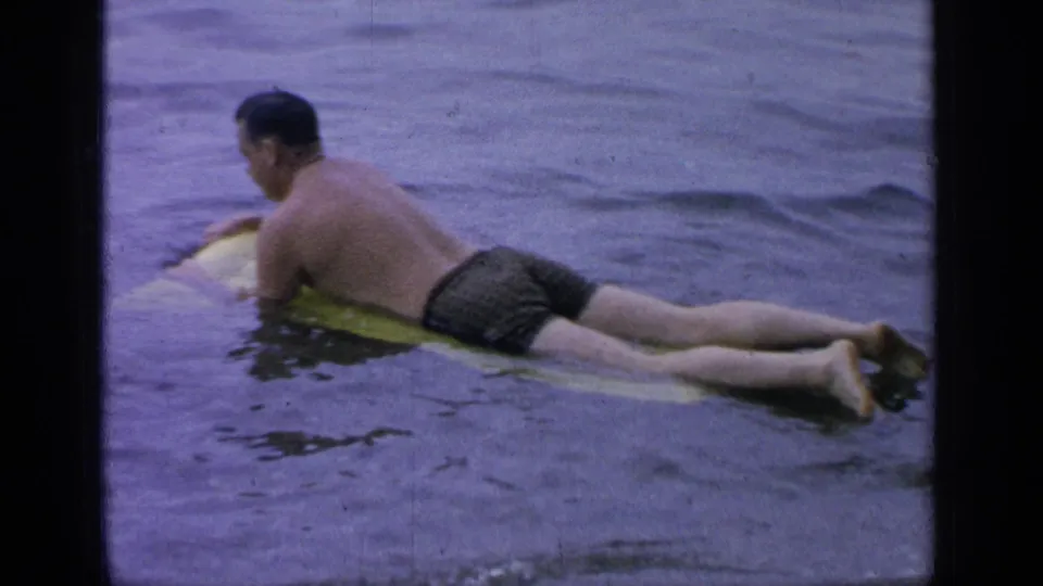 A side view shows the man lying on the yellow float or board, moving slowly across the lake surface.