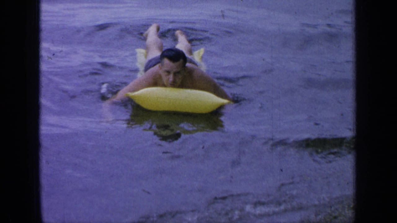 Adult man on a yellow inflatable raft drifts through Greenwood Lake water in 1964 home-movie footage.