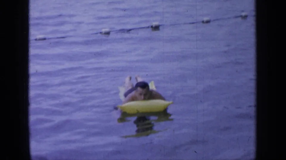 The man remains on the yellow raft with a buoy line visible behind him in Greenwood Lake water.