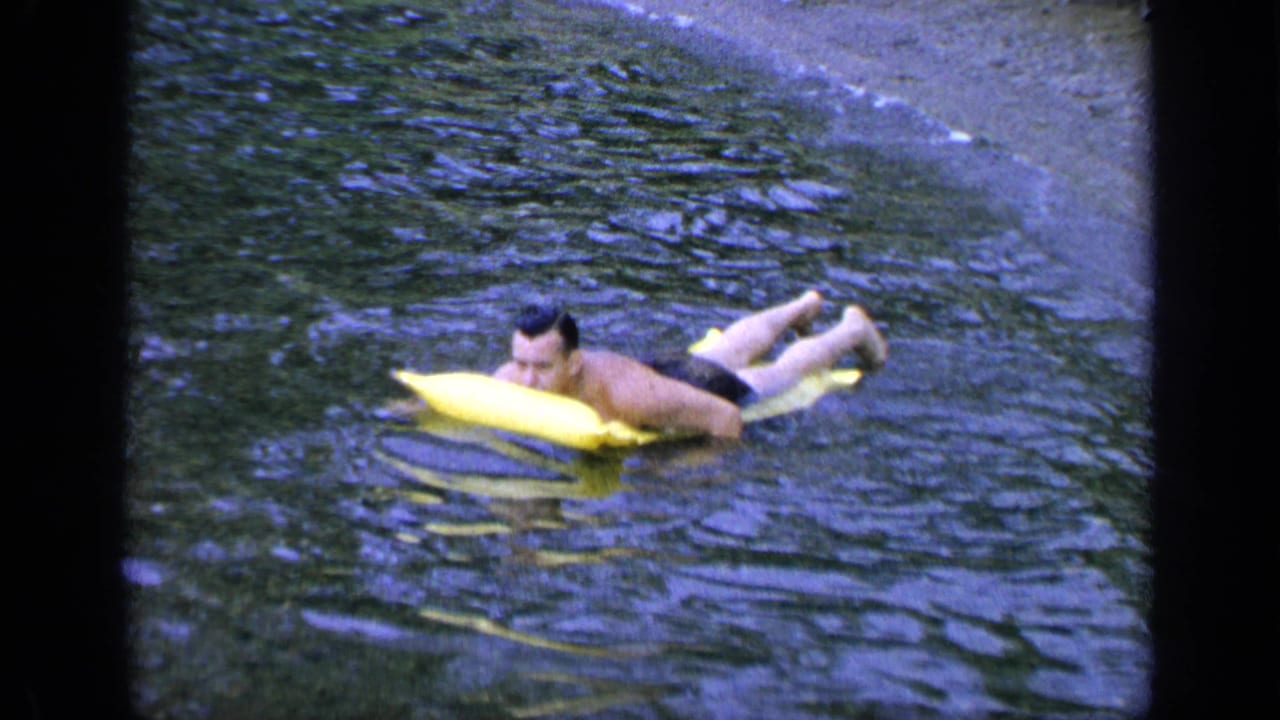 Man floating on a yellow inflatable board in lake water.