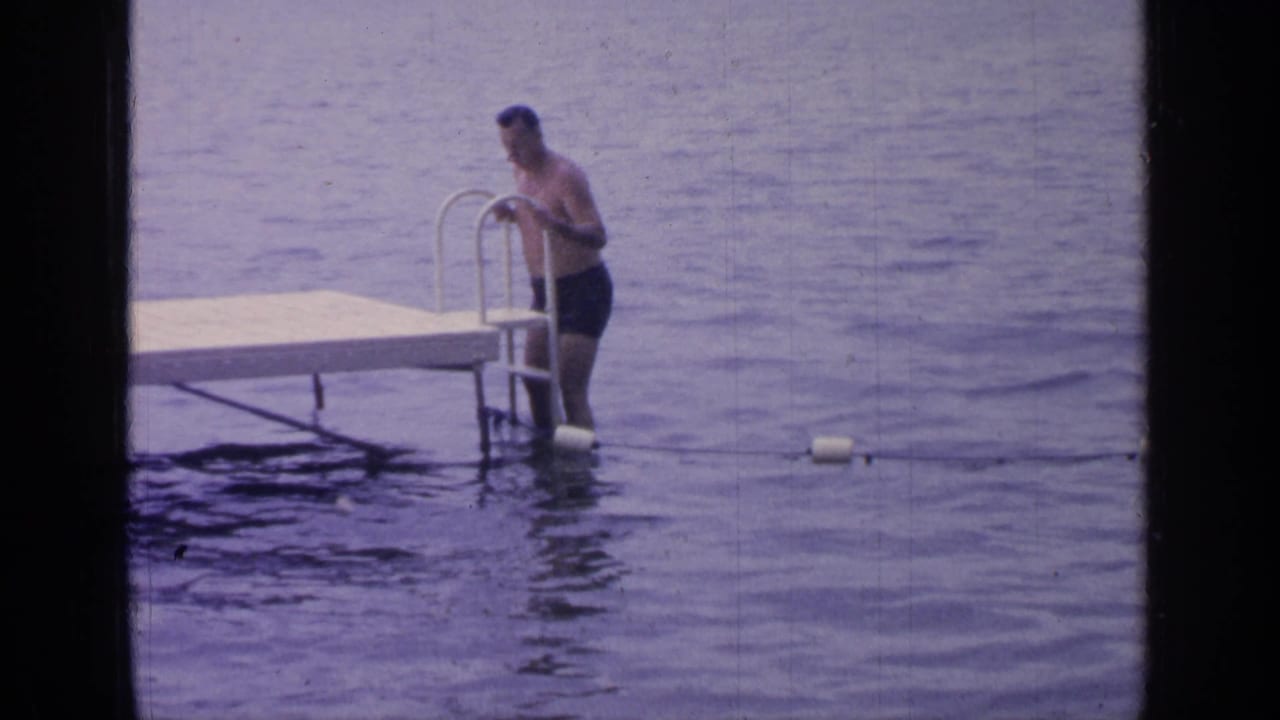 At Greenwood Lake in 1964, the man grips the metal ladder beside the dock while standing knee-deep in rippling water.