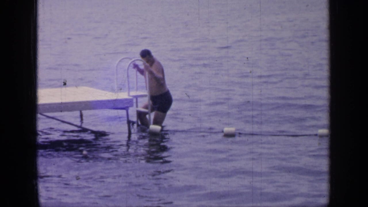 At Greenwood Lake in 1964, the man bends toward the metal ladder as he lowers himself beside the wooden dock into the lake.