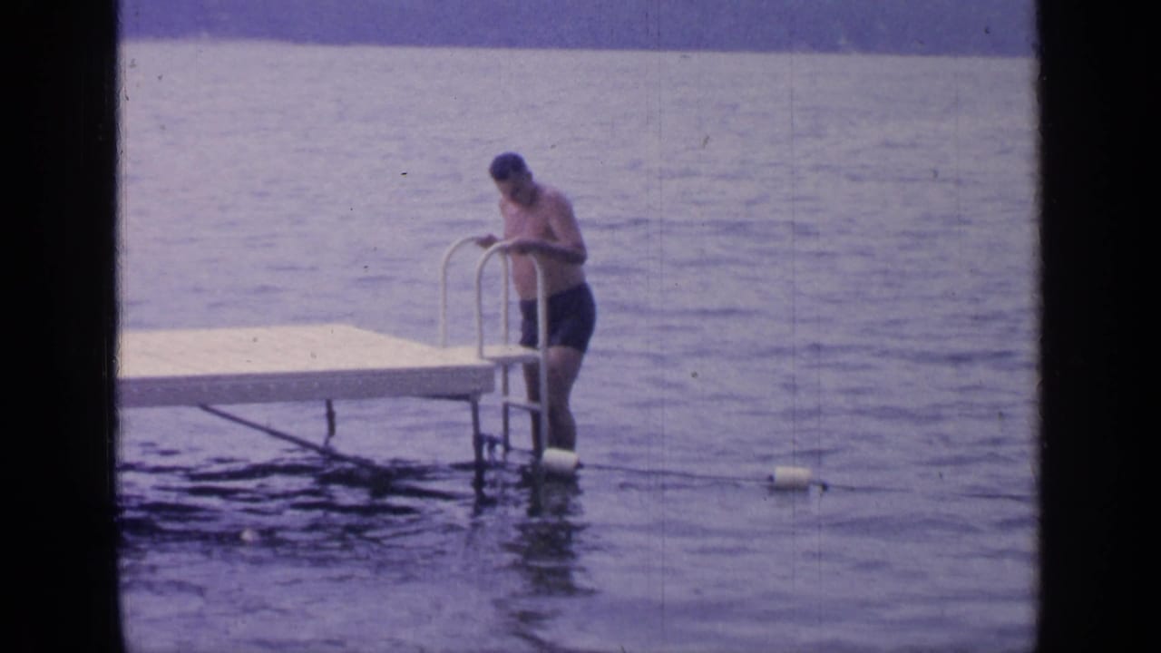 Man holds the dock ladder while standing in the lake beside the platform.