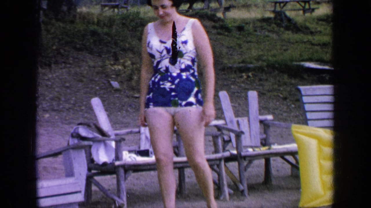 The woman in a blue floral swimsuit glances down as she stands near wooden chairs at Greenwood Lake, New York, in 1964.
