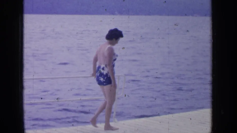 At Greenwood Lake in 1964, the woman walks barefoot along a wooden dock with open lake water behind her.