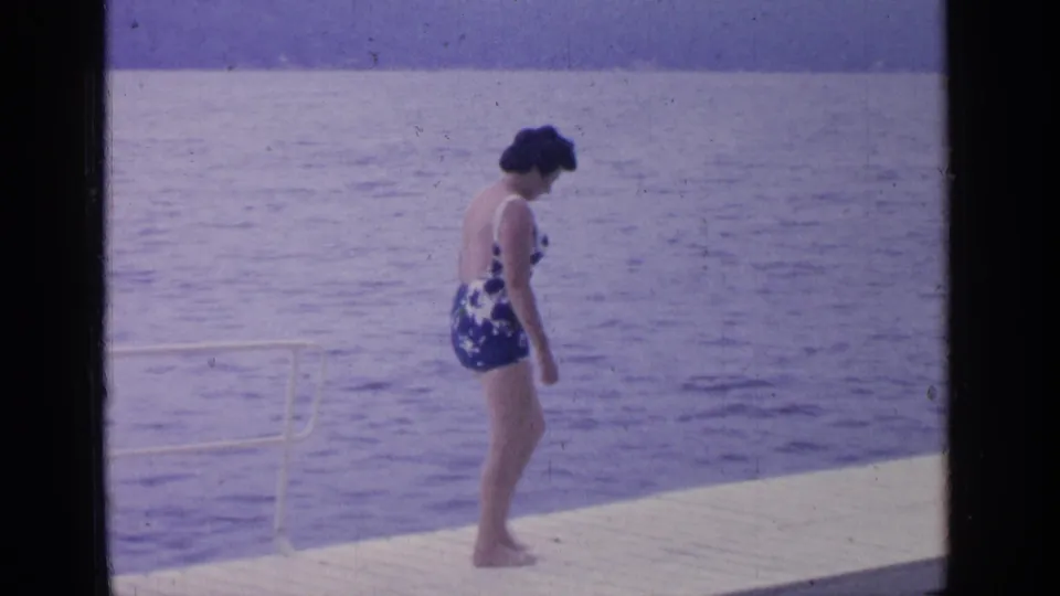 At Greenwood Lake in 1964, the woman continues along the dock, seen in profile against the lake surface.
