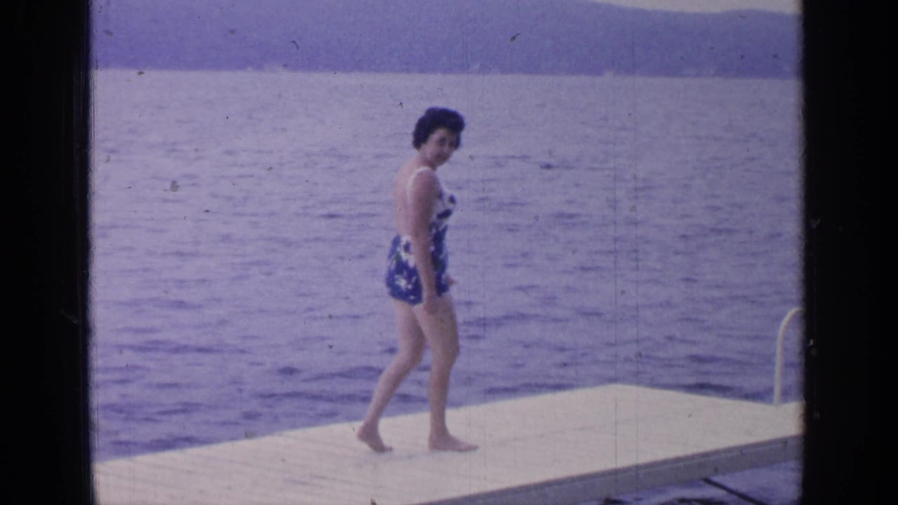 Woman continues along the dock with lake water and hills behind her.