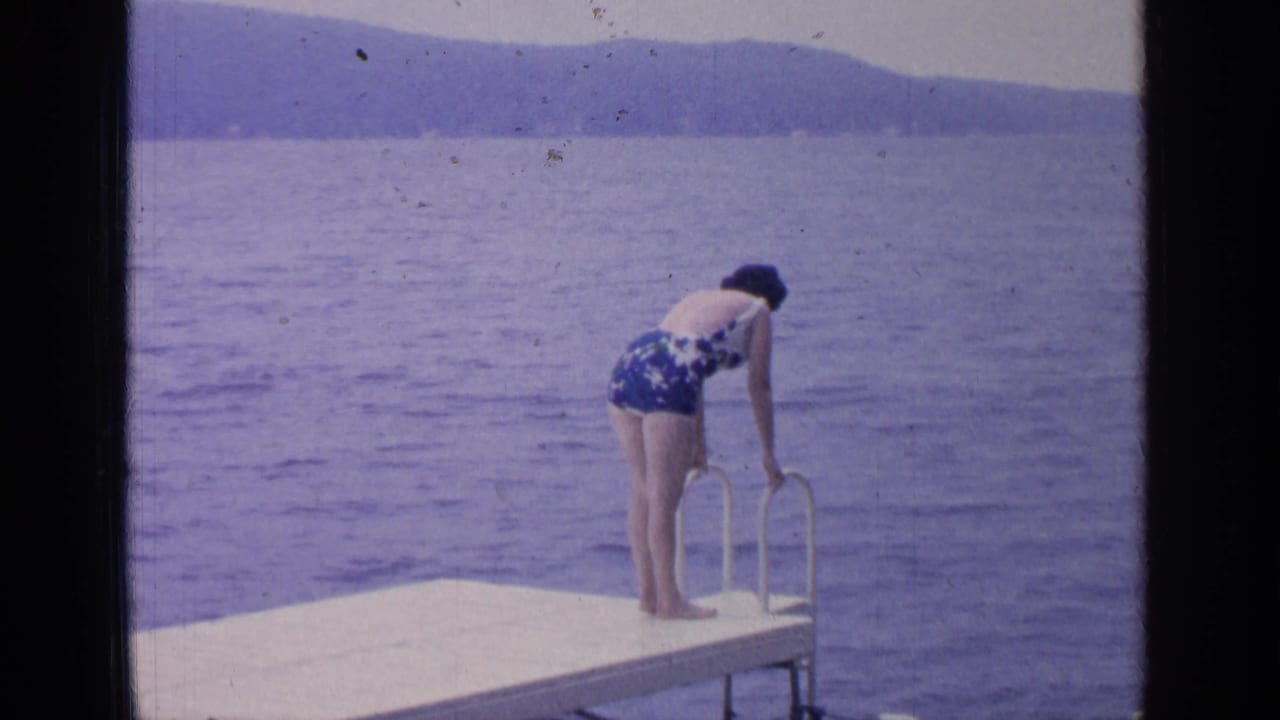 Woman bends forward to hold the dock ladder over the lake.