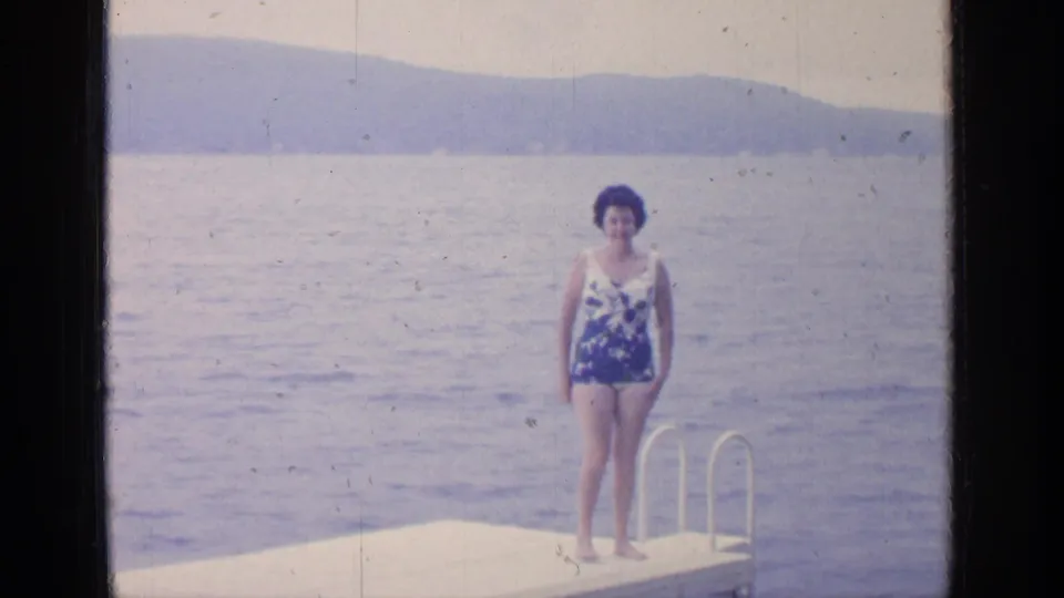 At Greenwood Lake in 1964, the woman faces the camera on the dock, with a metal ladder, lake water, and hills behind her.