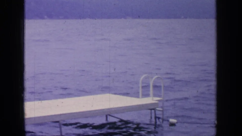 The final 1964 Greenwood Lake frame shows a white dock and metal ladder rails over rippled water with low hills in the background.