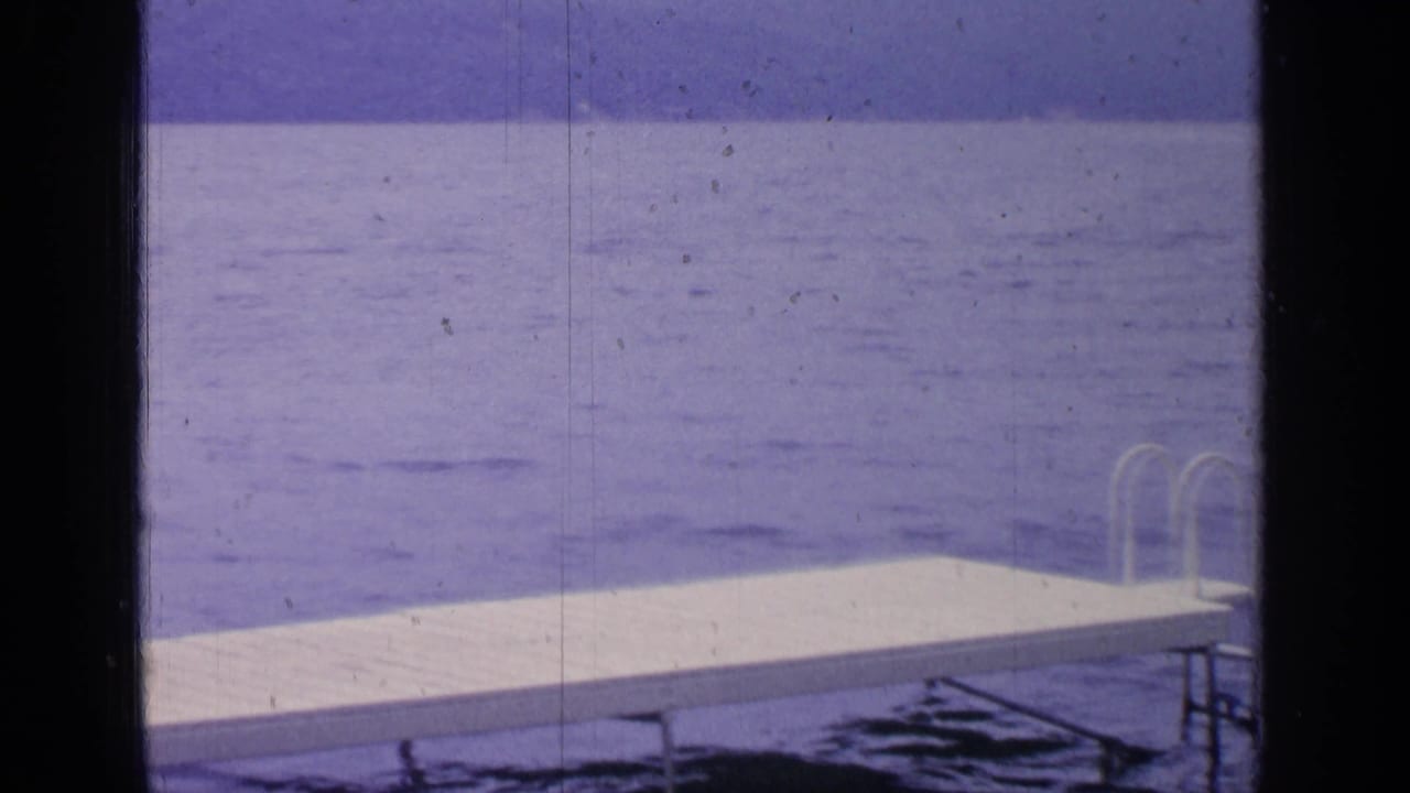 White dock and ladder beside calm blue lake water, framed by dark film borders.