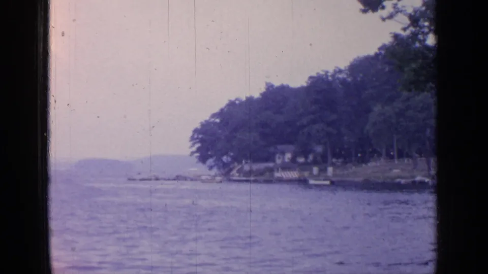 Greenwood Lake view with calm water, wooded shoreline, small boats, and distant hills in soft 8mm color.