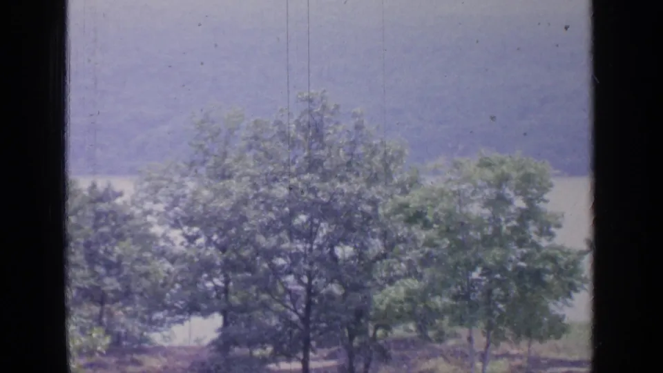 A similar 1964 Greenwood Lake view shows trees near the shoreline, with hazy hills and water seen through a dark window frame.