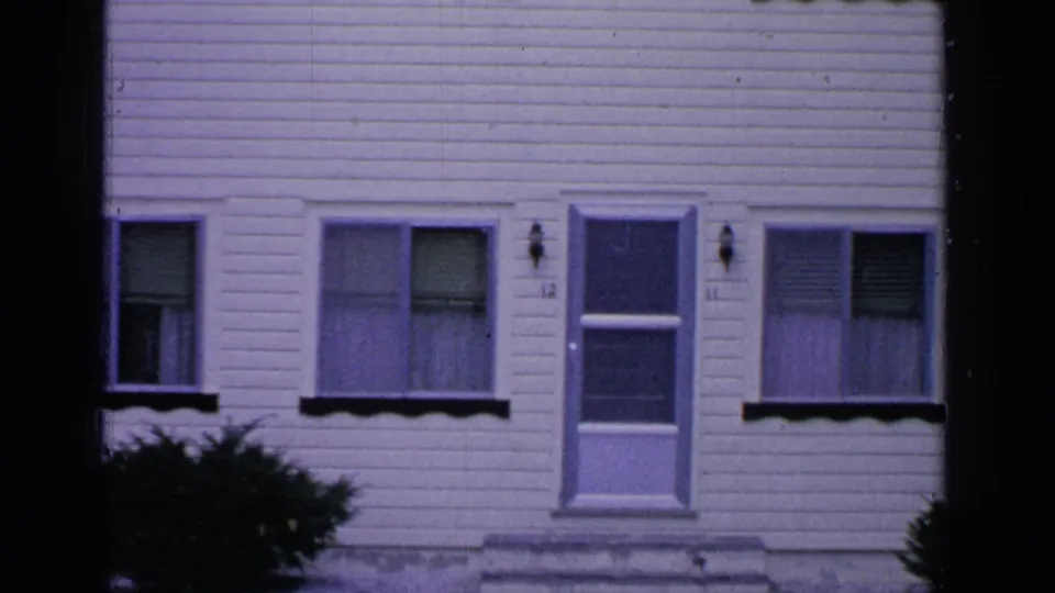 1964 Greenwood Lake frame with the white clapboard house centered on a door, windows with blinds, and shrubs below.