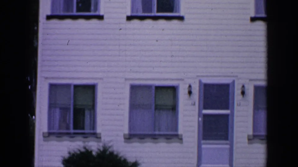 1964 Greenwood Lake home-movie frame showing the lower house facade with windows, blinds, door, and shrubbery.