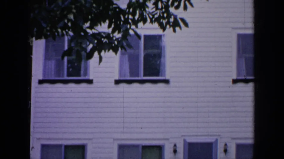 1964 Greenwood Lake frame showing a white clapboard house wall, several windows, and tree branches entering the view.