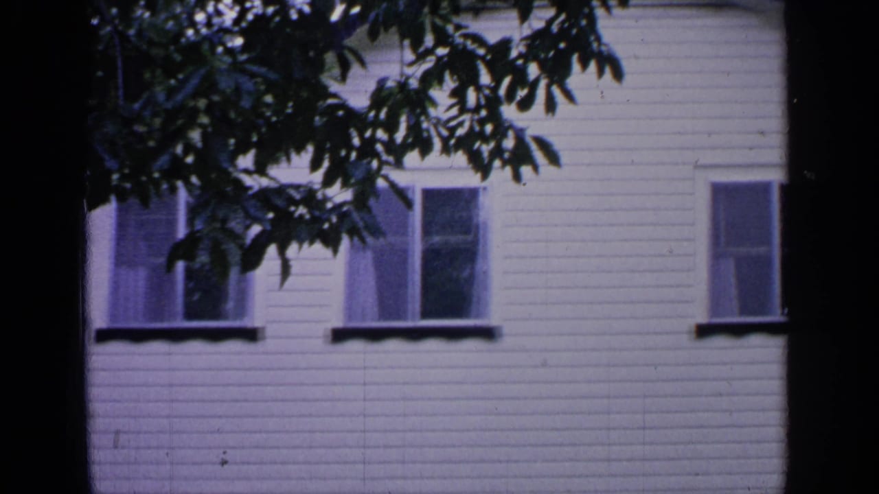 White clapboard house facade with upper windows partly framed by dark tree branches.
