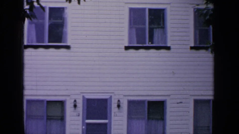 1964 Greenwood Lake residential exterior showing a central front door, adjacent windows, lamps, and clapboard siding in 8mm color.