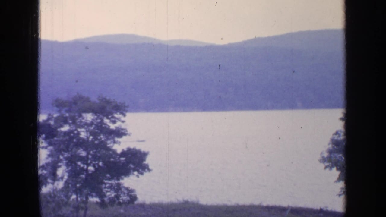 Lake and distant mountains seen past foreground trees and dark film borders.