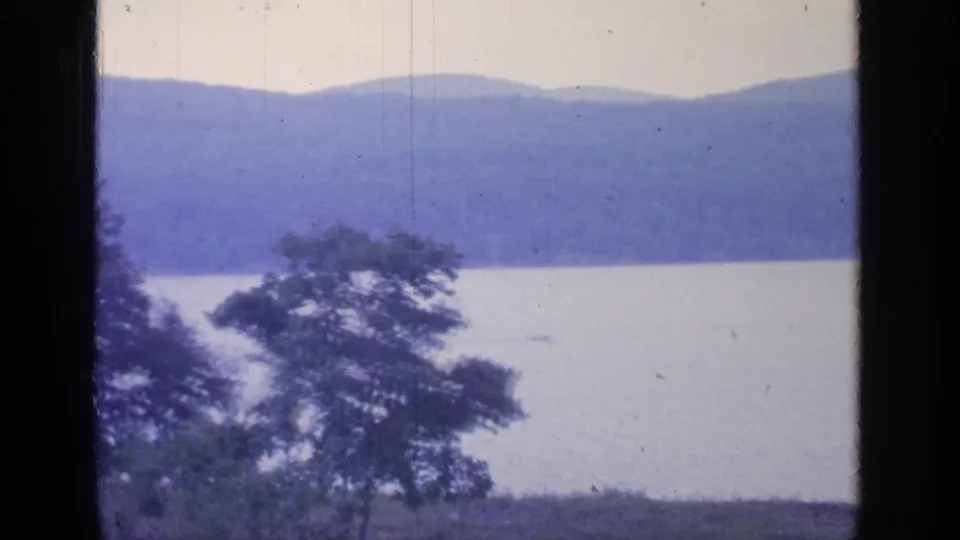 Greenwood Lake in 1964, showing a foreground tree, still water, distant blue mountains, and soft faded 8mm color.