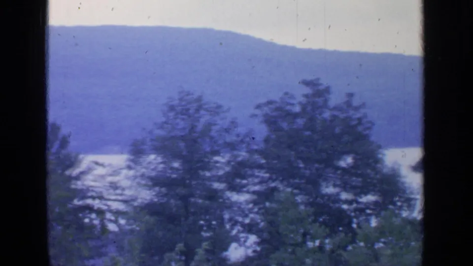 Likely Greenwood Lake, New York, in 1964, seen as a quiet 8mm landscape through dark framing with trees and mountains.