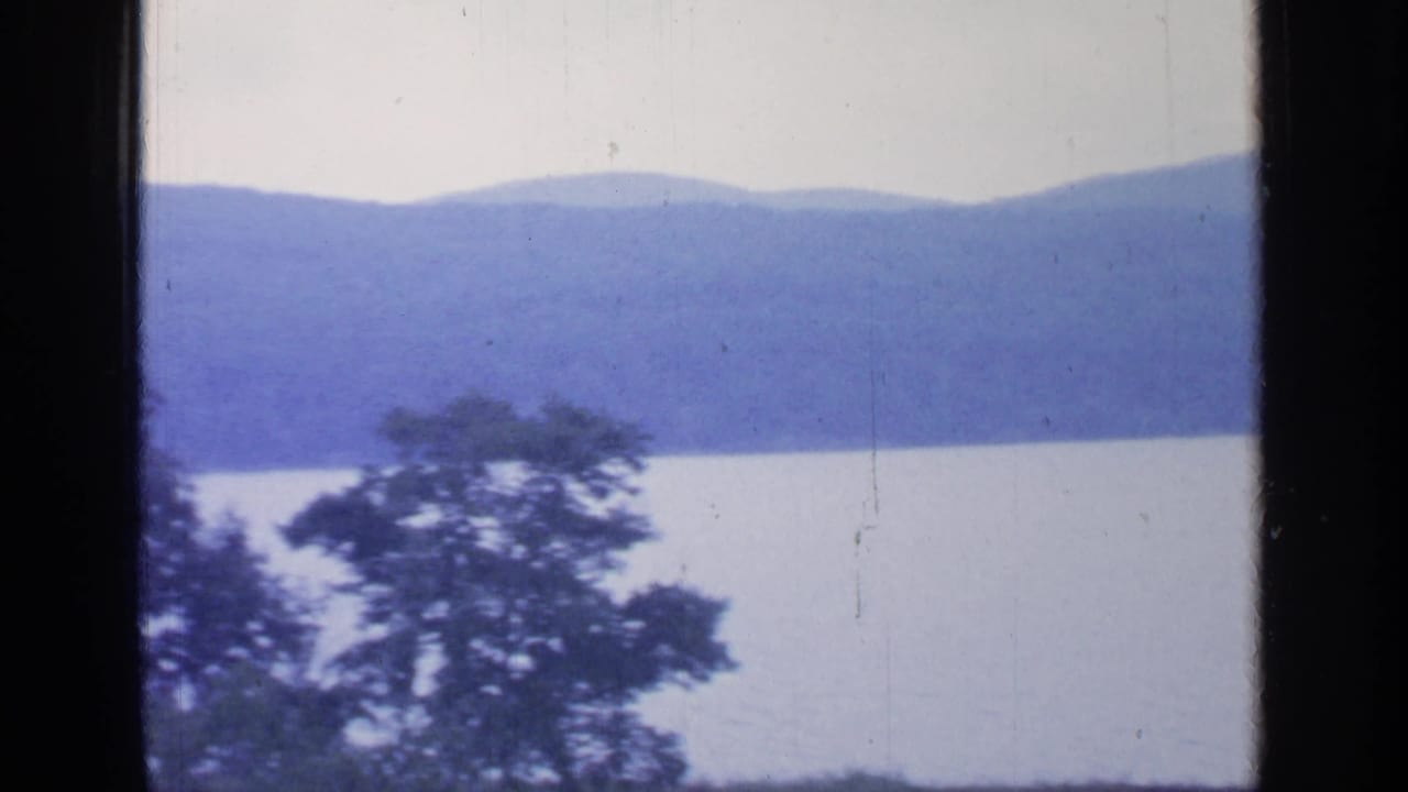 Greenwood Lake landscape with layered blue hills, still water, foreground trees, and a dark central film divider.