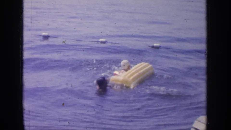 At Greenwood Lake in 1964, the yellow raft tips as two adults move through the water near a line of white buoys.