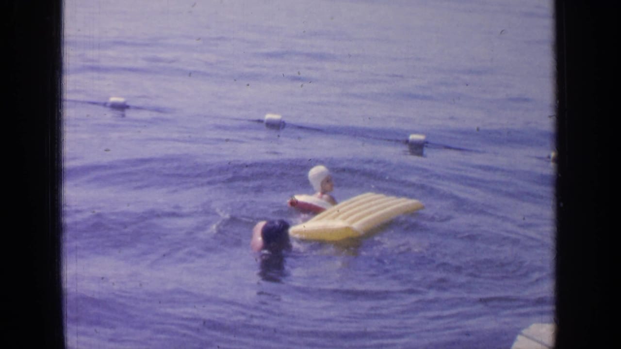 Two swimmers in lake water near a yellow inflatable raft and buoy line.