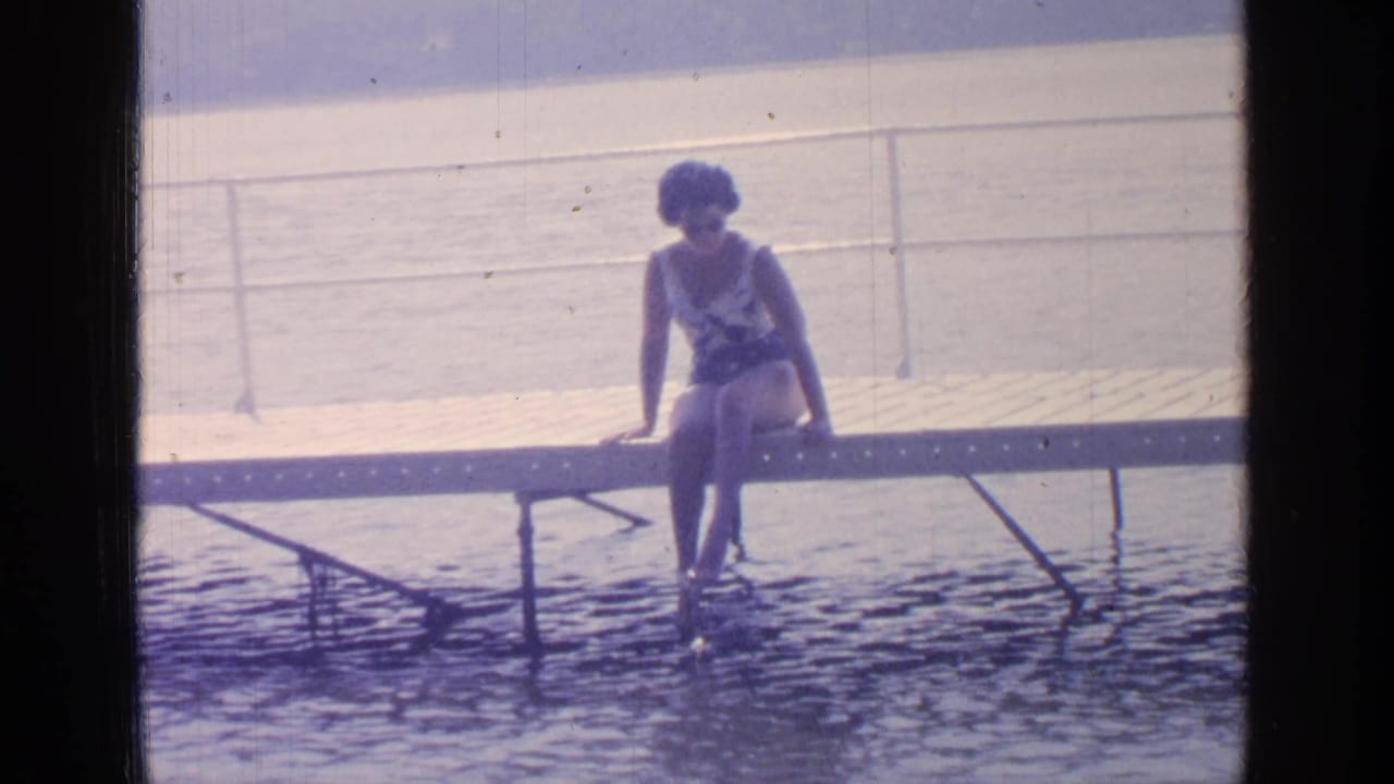 Woman in a swimsuit sitting on a dock with her feet near the lake water.