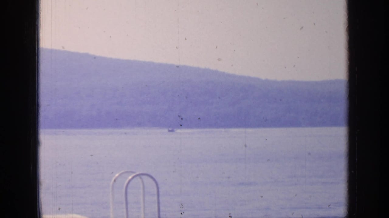 Small boat on a lake beyond a dark window frame and distant hills.