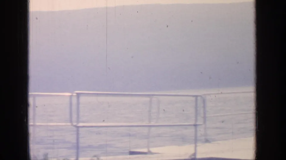 Greenwood Lake home-movie frame with a waterfront railing, dock edge, calm water, and hazy hills in soft 8mm color.