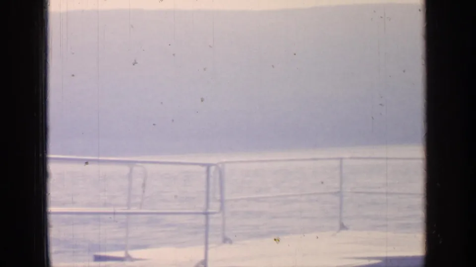 Greenwood Lake waterfront view on 8mm film, showing railing, sunlit water, and hazy hills in the distance.