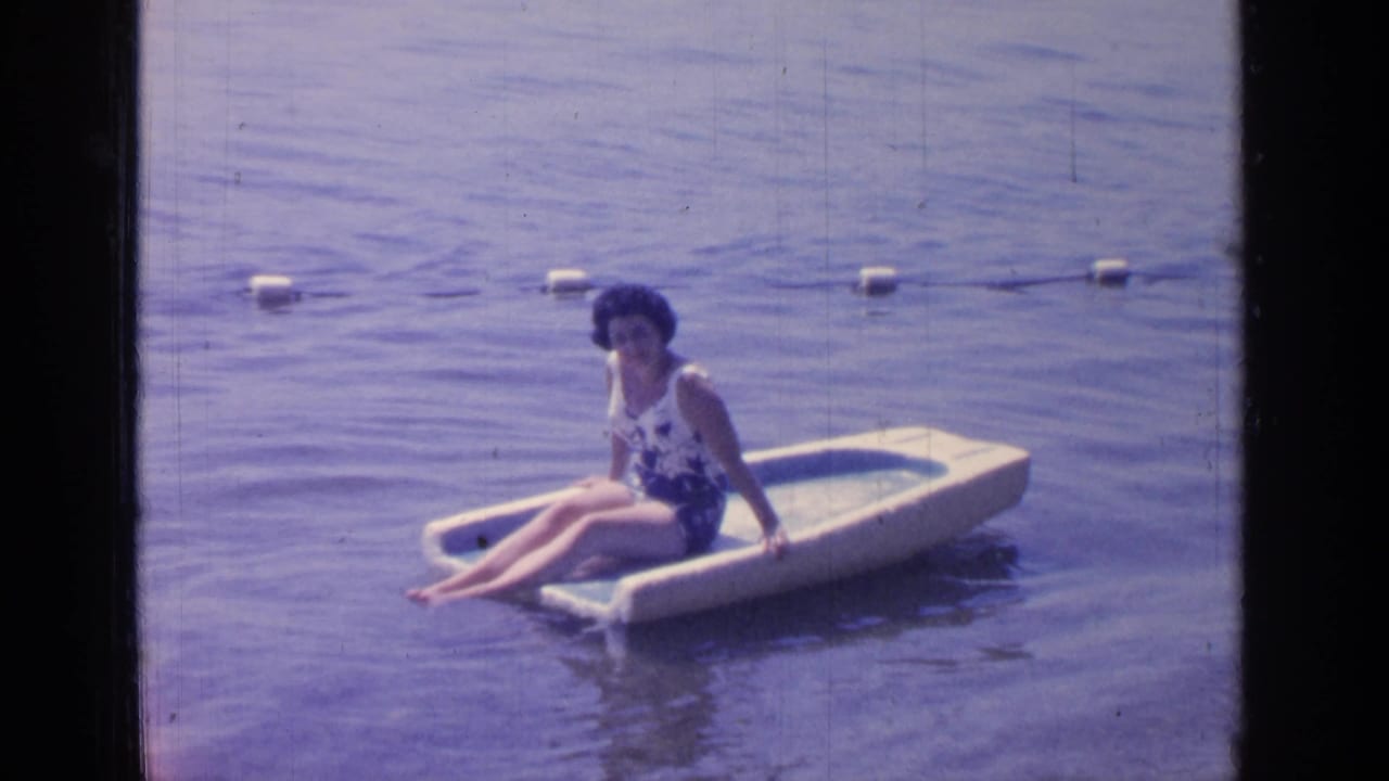 Woman seated on a pale float with buoys behind her in calm water.