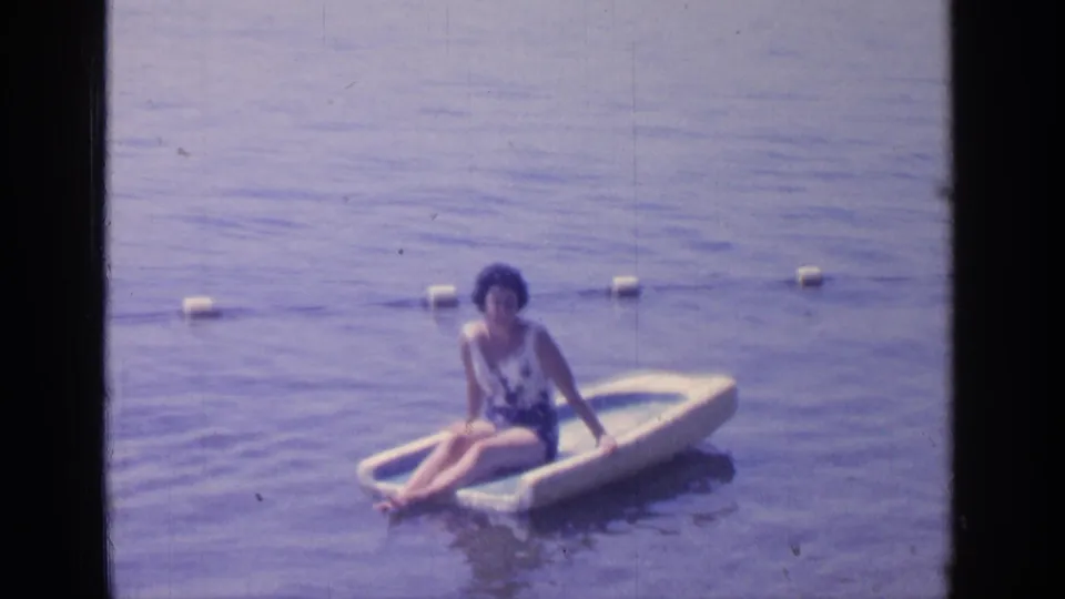 The woman leans back on the small raft at Greenwood Lake, her legs extended over the front as the water stays calm around her.