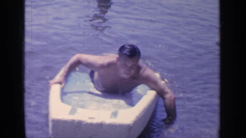 The adult man sits higher on the foam float, with one arm extended into the lake as he practices movement.