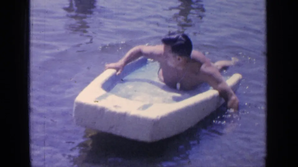 The man grips the white float and paddles in the lake, creating small splashes around the frame.